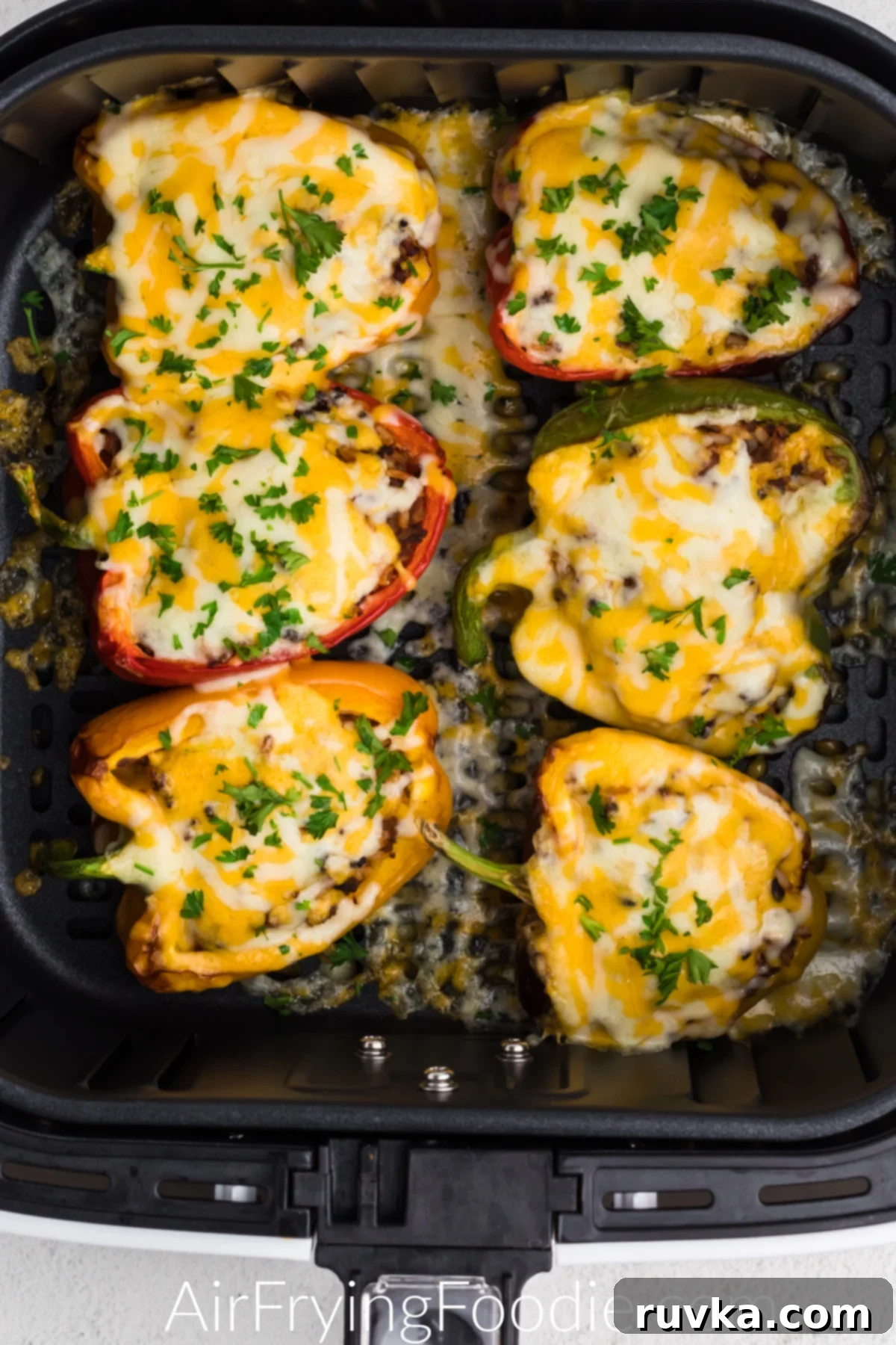 Effortless Air Fryer Stuffed Peppers 5 Stuffed peppers topped with cheese and fresh parsley in the basket of the air fryer.
