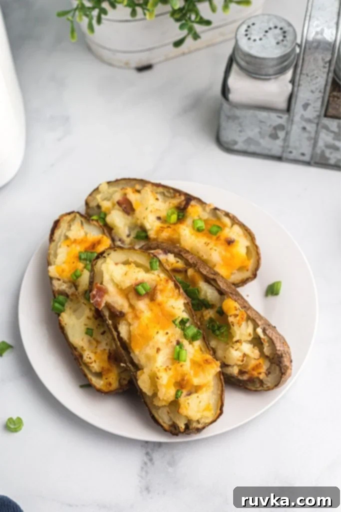Ultimate Air Fryer Twice Baked Potatoes 2 Twice baked potatoes on a white plate sprinkled with chopped green onions.
