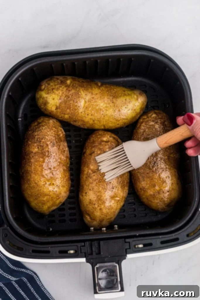 Ultimate Air Fryer Twice Baked Potatoes 4 Brushing olive oil onto potatoes before cooking in the air fryer basket.