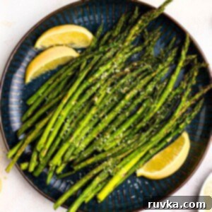 Air Fryer Thanksgiving Feast Made Easy 19 Green juicy asparagus on a black plate with lemon wedges.
