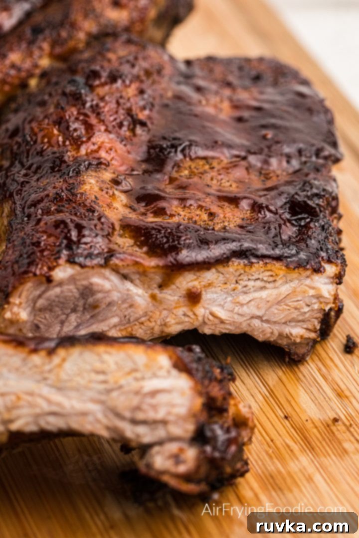 Ultimate Air Fryer BBQ Ribs 2 Air fryer ribs slathered in bbq sauce and sliced on a wooden cutting board, ready to be served.
