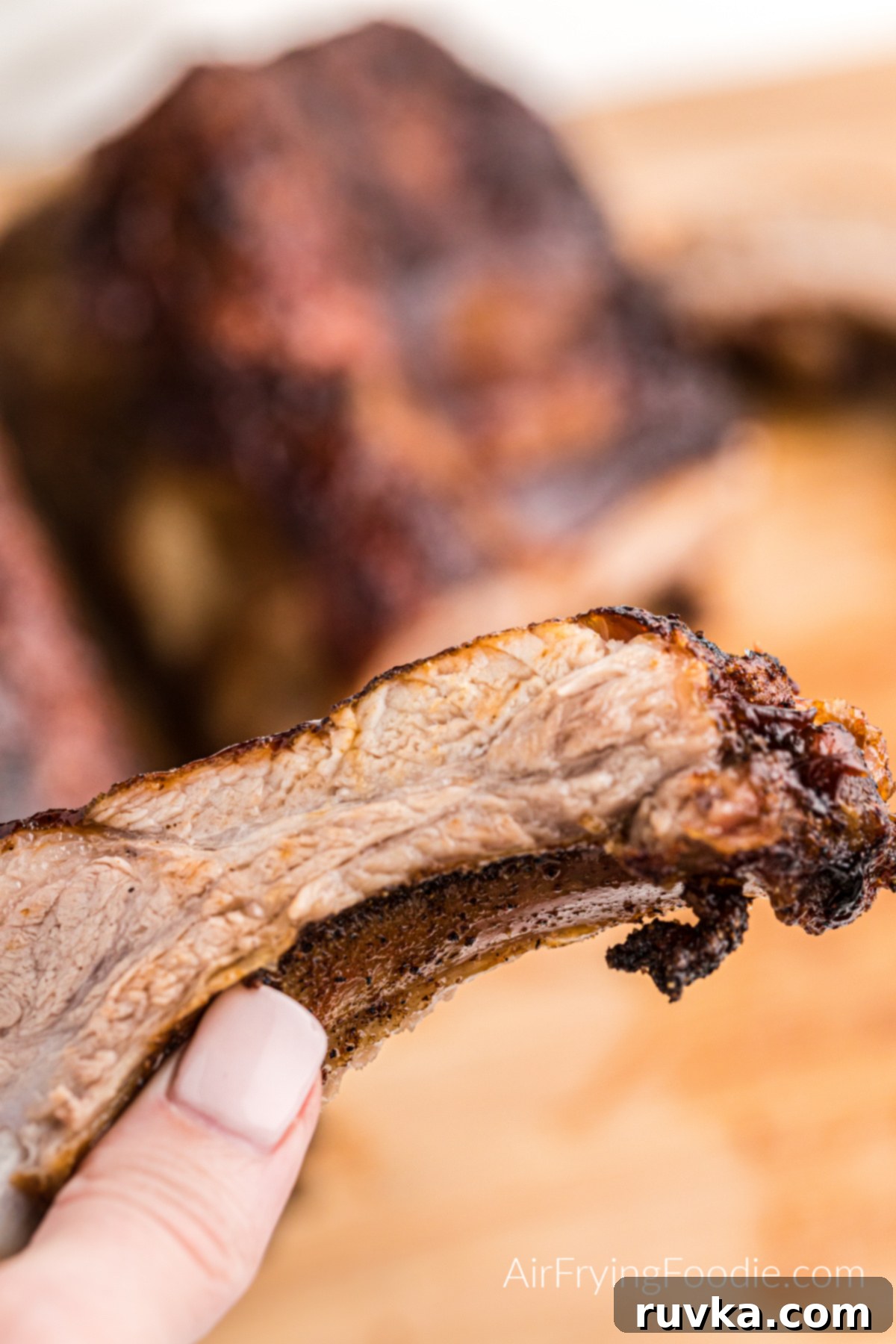 Ultimate Air Fryer BBQ Ribs 9 A hand holding an Air Fryer rib with BBQ sauce, showcasing its tenderness and delicious appearance.
