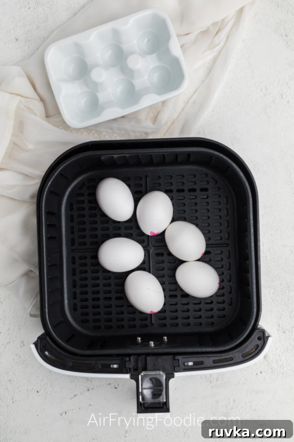 Boil-Free Hard Boiled Eggs in Your Air Fryer 4 Eggs in an air fryer basket on a white cloth.