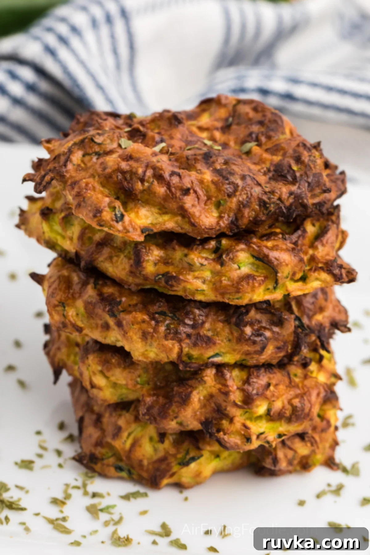Crispy Air Fryer Zucchini Fritters 2 Zucchini fritters stacked on a plate and topped with fresh parsley.