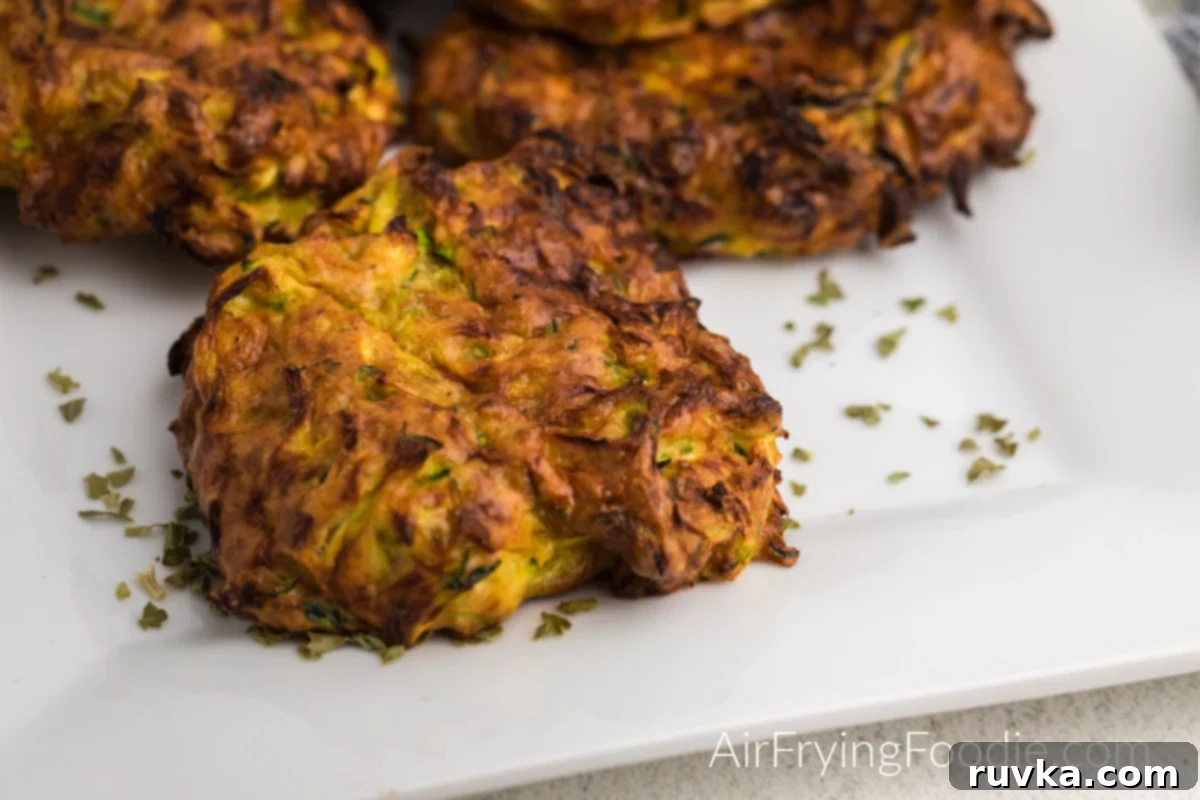 Crispy Air Fryer Zucchini Fritters 8 Delicious Zucchini fritters arranged on a white plate, garnished with fresh parsley flakes.