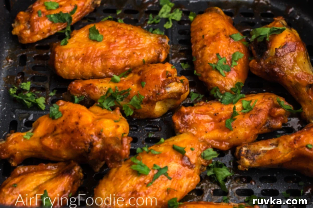 Crispy Air Fryer Chicken Wings 5 chicken wings in air fryer basket tossed in sauce and garnished with fresh parsley.