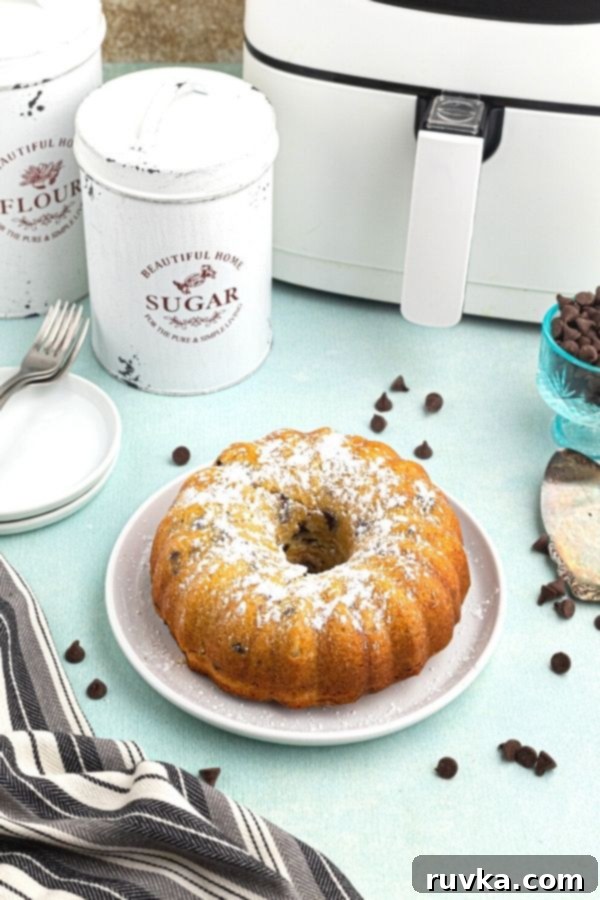 Air Fried Chocolate Chip Pound Cake 5 Baked pound cake served on a white plate, whole, sprinkled with powdered sugar and chocolate chips scattered around the plater.
