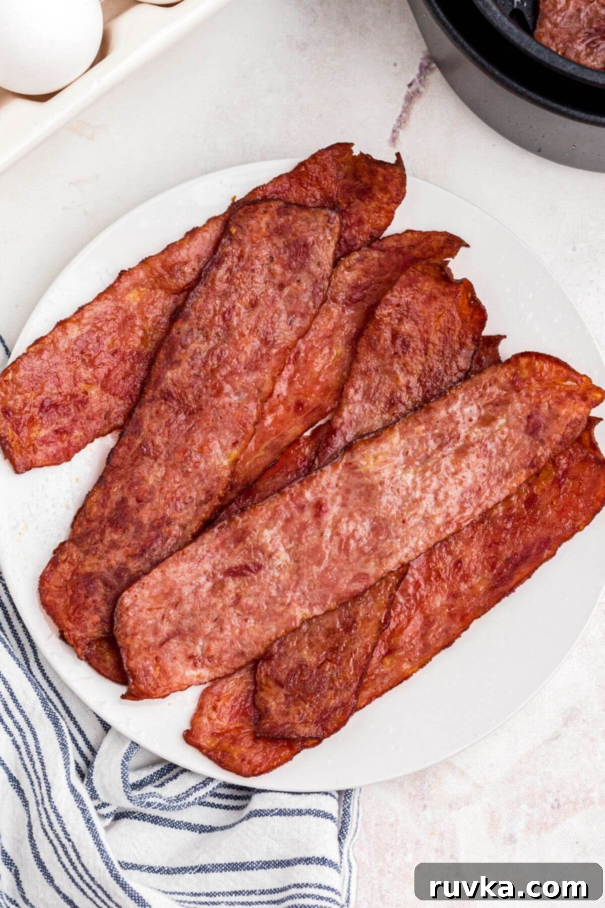 Crispy Air Fryer Turkey Bacon 2 Juicy pieces of turkey bacon stacked on a white round plate, ready to be enjoyed.