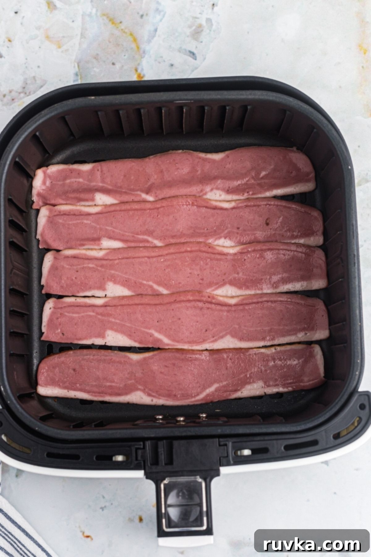 Crispy Air Fryer Turkey Bacon 4 Uncooked turkey bacon strips laid out in a single layer in the air fryer basket.