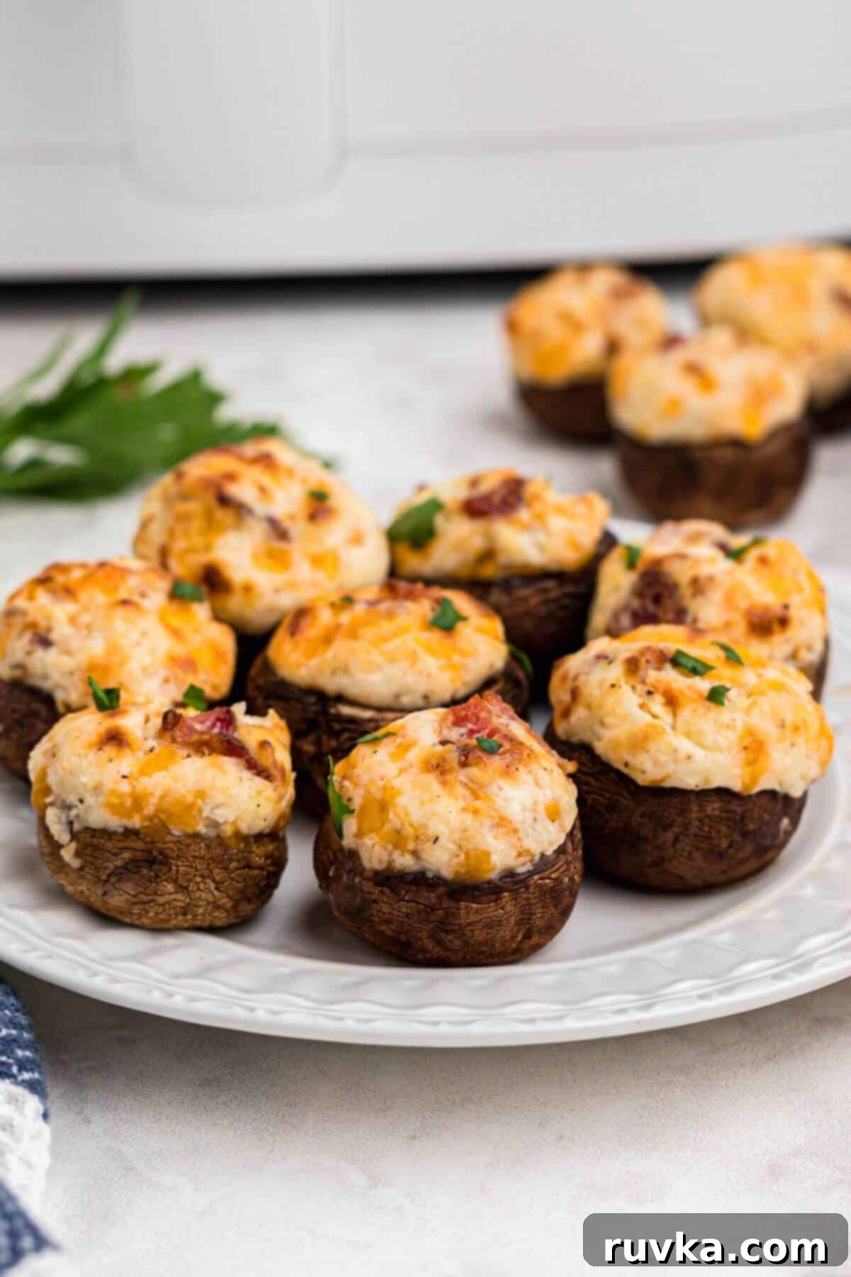 Ultimate Air Fryer Stuffed Mushrooms 2 Golden brown stuffed mushrooms filled with cream cheese, cheese, and bacon, on a small white plate.