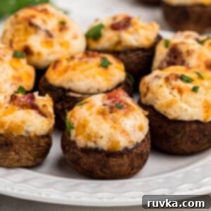 Ultimate Air Fryer Stuffed Mushrooms 9 Brown mushroom caps stuffed with cream cheese, cheese, and bacon, and seasonings on a small white plate.