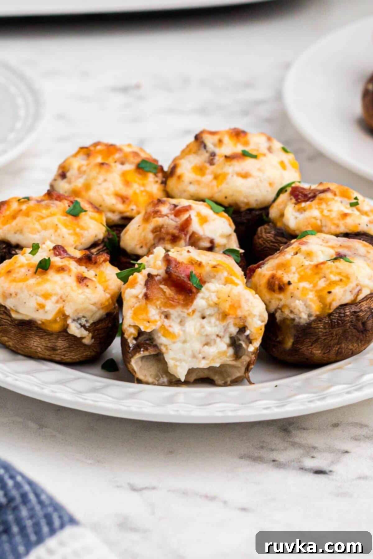 Ultimate Air Fryer Stuffed Mushrooms 8 Golden brown mushrooms stuffed with cream cheese, cheddar cheese and bacon, on a small white plate.