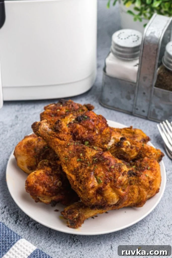 Crispy Air Fryer Drumsticks 2 Plate of crispy chicken drumsticks stacked on a white plate on a light blue table.
