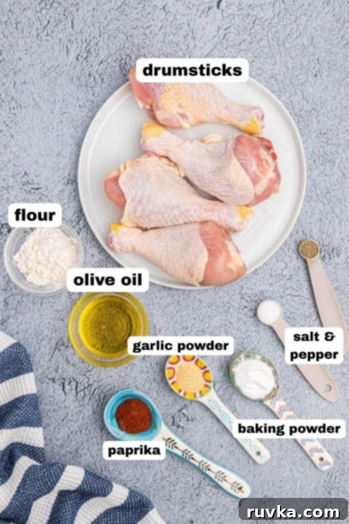 Crispy Air Fryer Drumsticks 3 Ingredients needed to make drumsticks, seasonings, olive oil, and uncooked chicken, in dishes and measuring spoons, on a light gray table.
