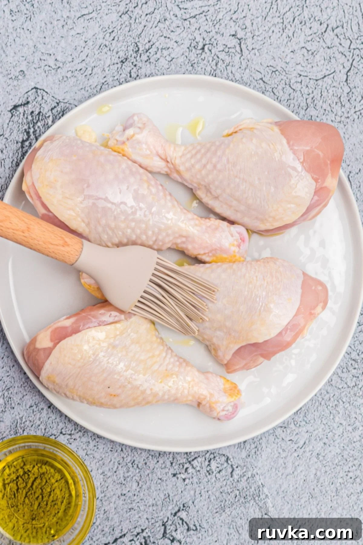 Crispy Air Fryer Drumsticks 4 Brushing uncooked drumsticks with olive oil on a white plate.