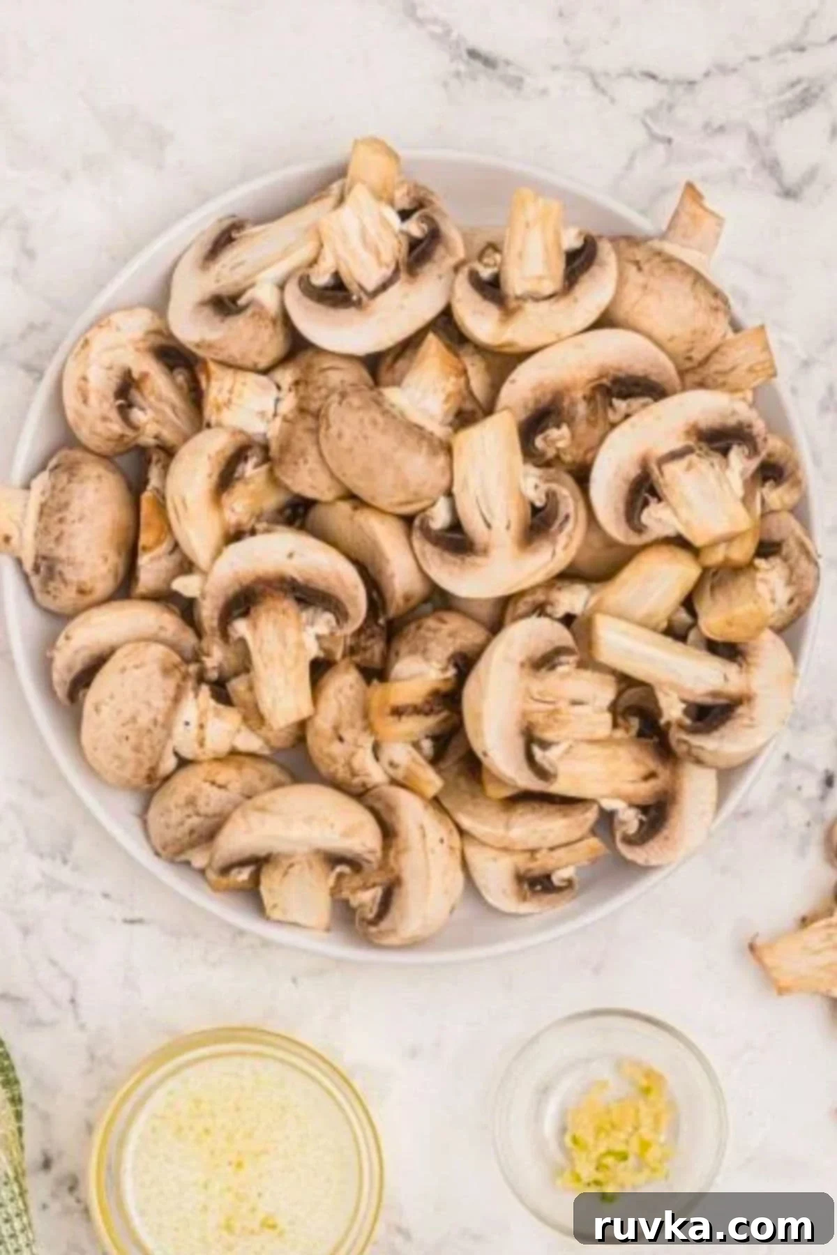 Perfectly Crispy Air Fryer Mushrooms 4 White mushrooms being sliced and placed in a large clear glass bowl.