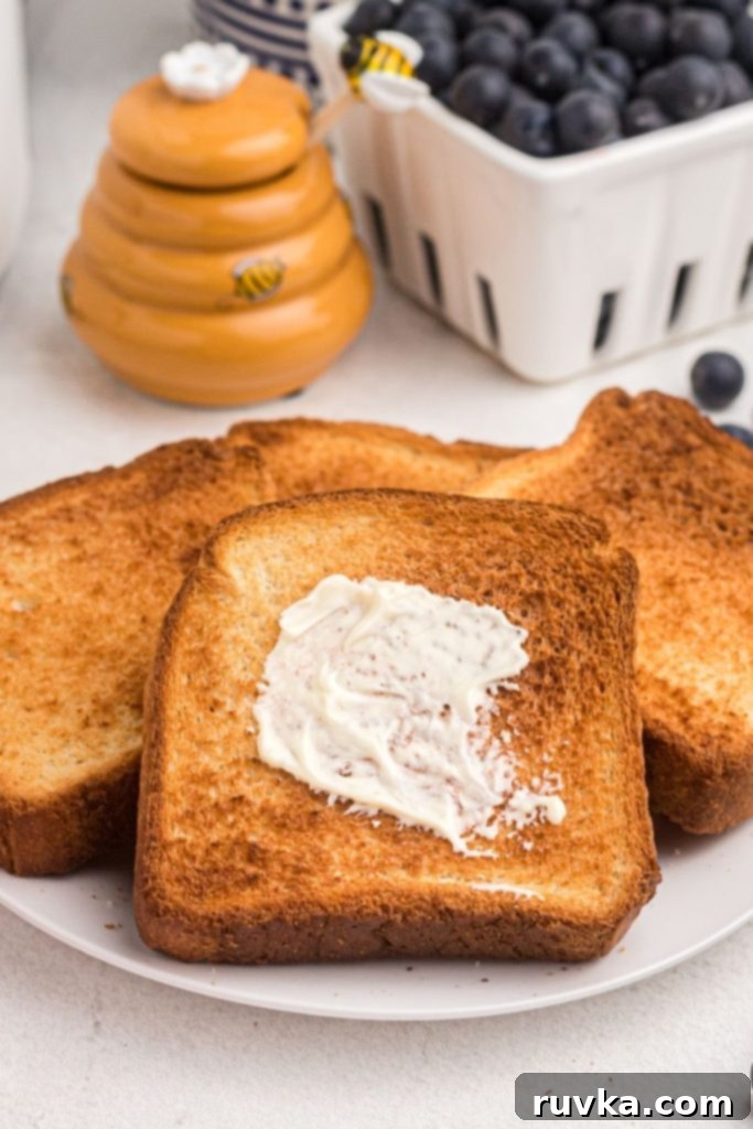 The Ultimate Air Fryer Toast 2 Golden toast on a white plate with honey and blueberries on the table