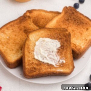 The Ultimate Air Fryer Toast 7 Golden toast with one being buttered. Served on a white plate with blueberries and butter.
