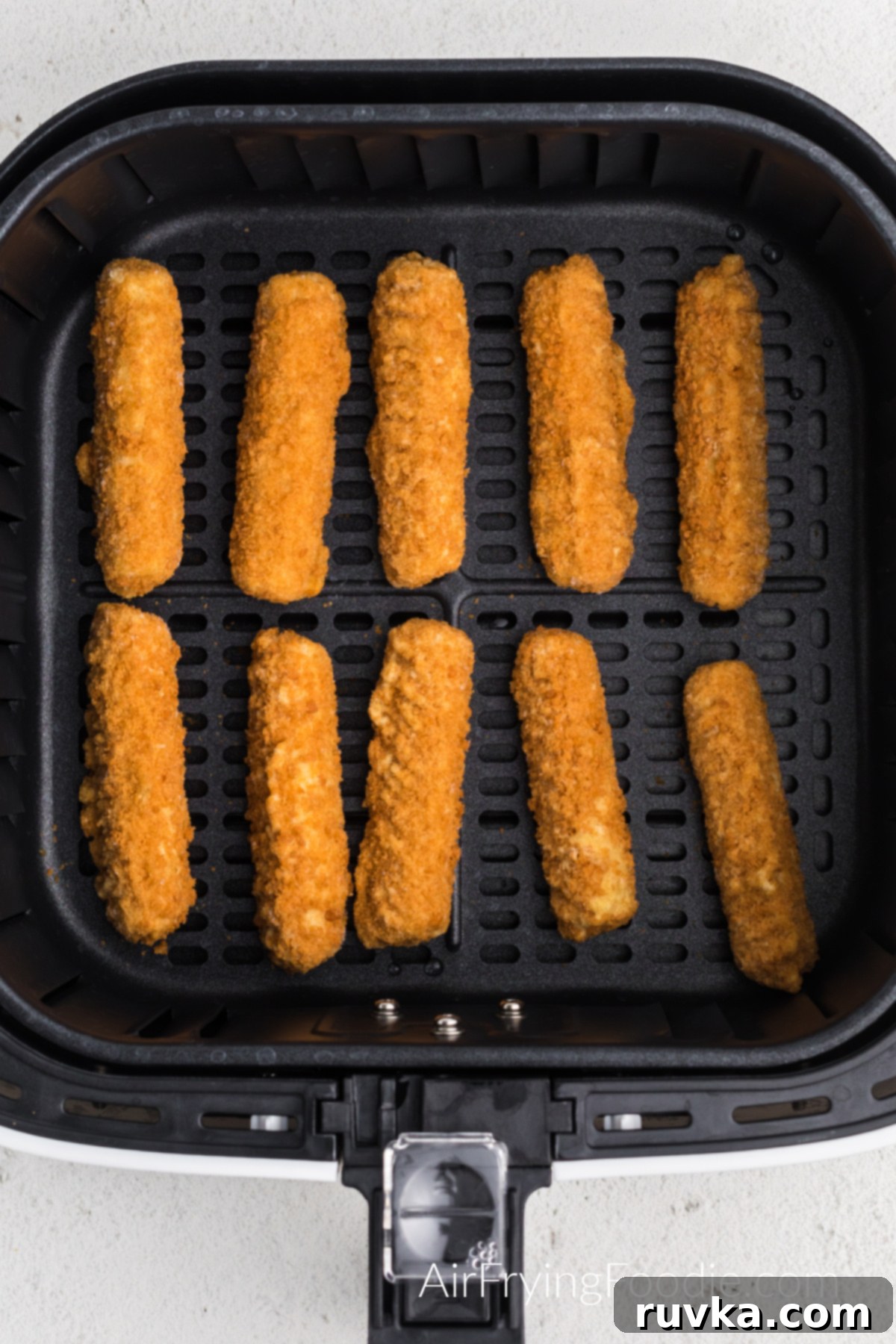 Crispy Air Fryer Mozzarella Sticks 5 Frozen mozzarella sticks placed in a single layer in the air fryer basket ready to cook.