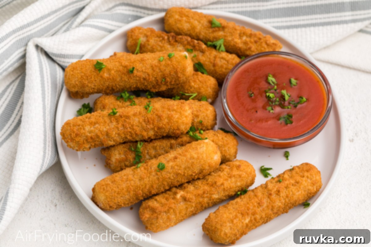 Crispy Air Fryer Mozzarella Sticks 6 Mozzarella cheese sticks that were frozen and then air fried - placed on a white plate and topped with fresh parsley.