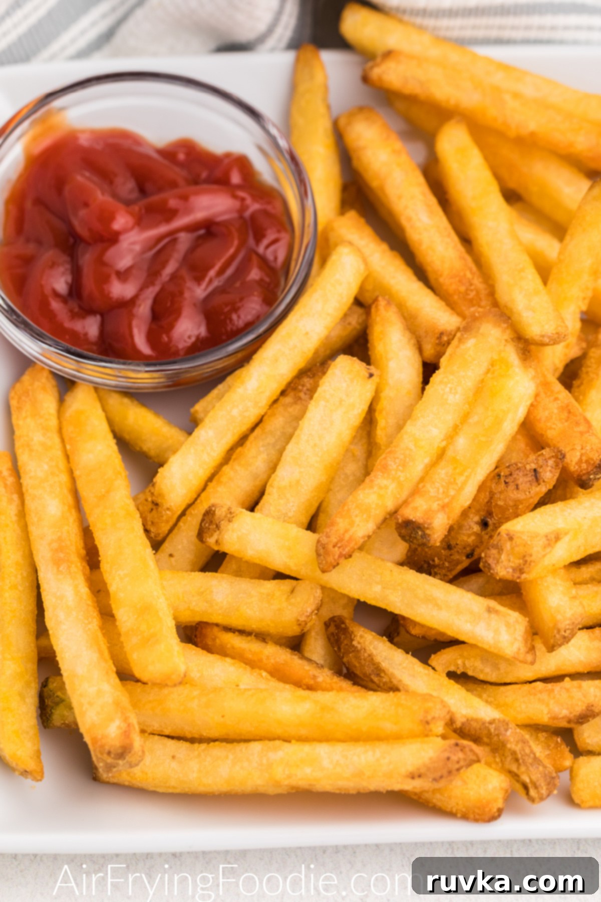 Crispy Air Fryer Frozen French Fries 6 Close-up shot of crispy air-fried French fries on a white plate with a side of ketchup, ready to be enjoyed.