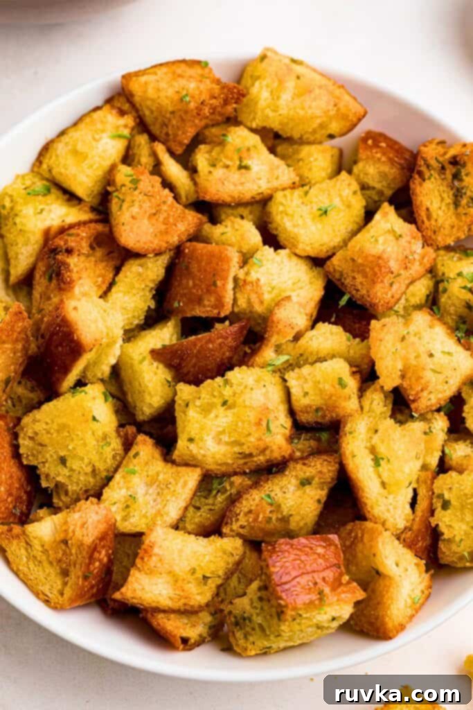 Perfectly Crispy Air Fryer Croutons 2 Seasoned golden croutons in a white bowl on a marble table next to a salad.
