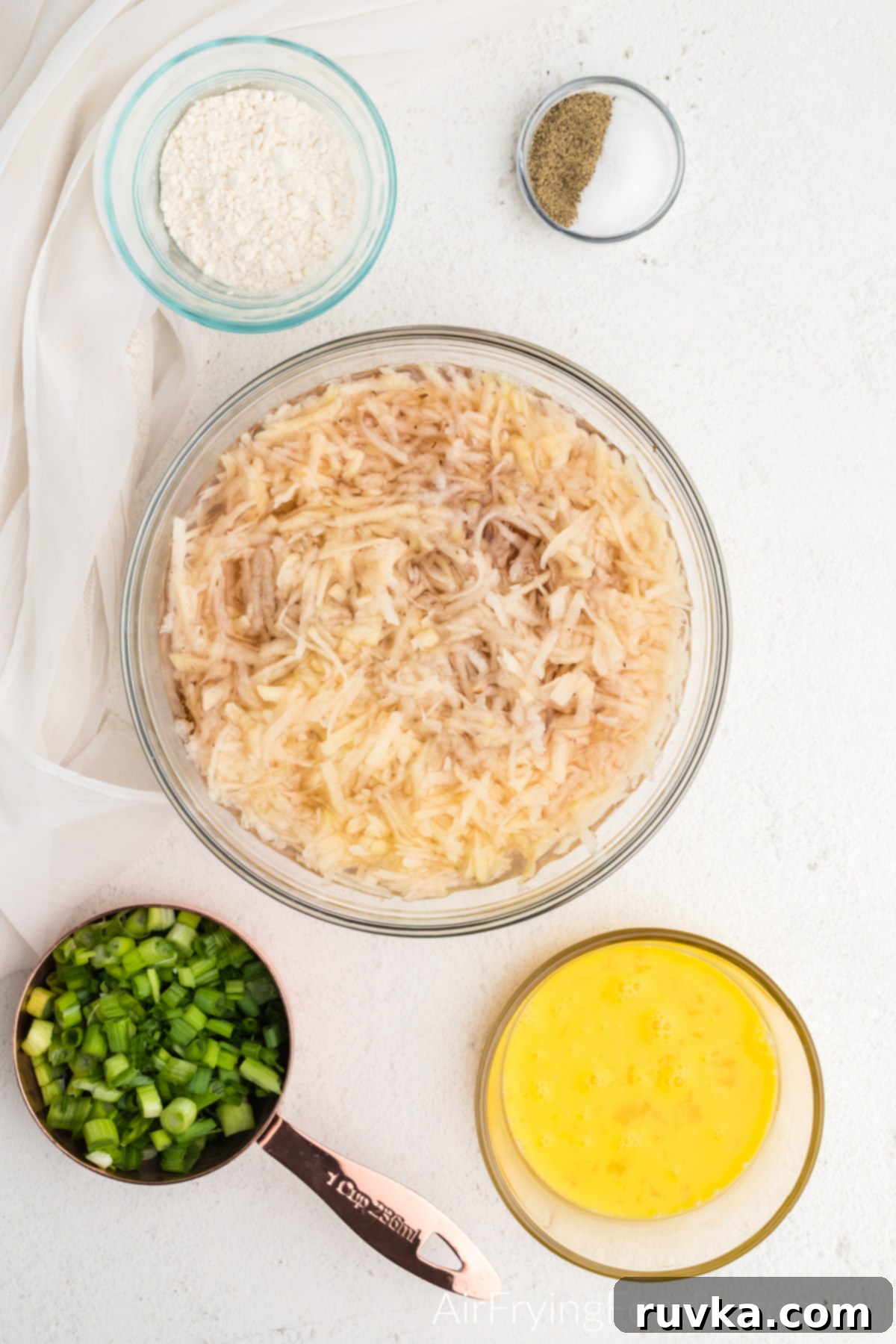 Crispy Air Fryer Latkes 4 shredded potato soaking in a bowl of water surrounded by additional ingredients.