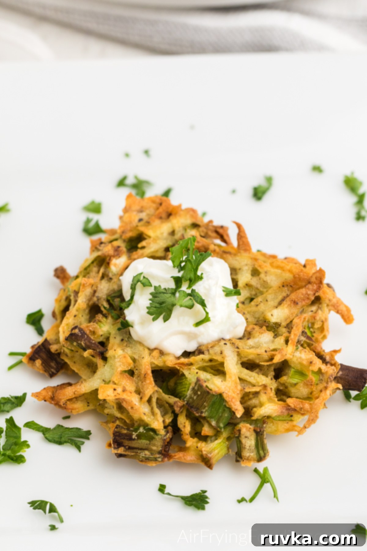 Crispy Air Fryer Latkes 9 Latke on a white plate ready to eat and garnished with sour cream and parsley.