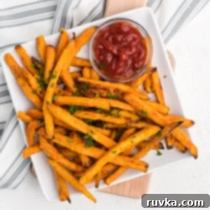 Frozen sweet potato fries made in the air fryer - fully cooked and served on a white plate with a side of ketchup.