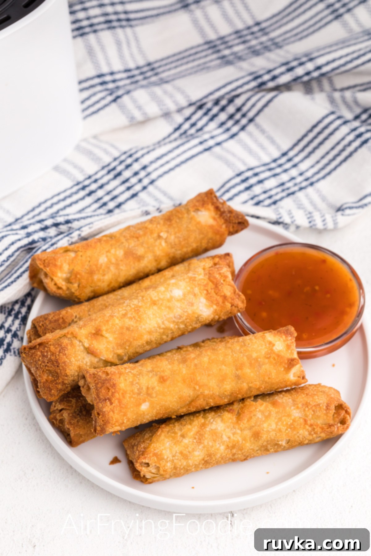 Crispy Frozen Egg Rolls in Air Fryer 2 Frozen egg rolls that have been fully cooked in the air fryer. Served on a white plate with Thai chili sauce.