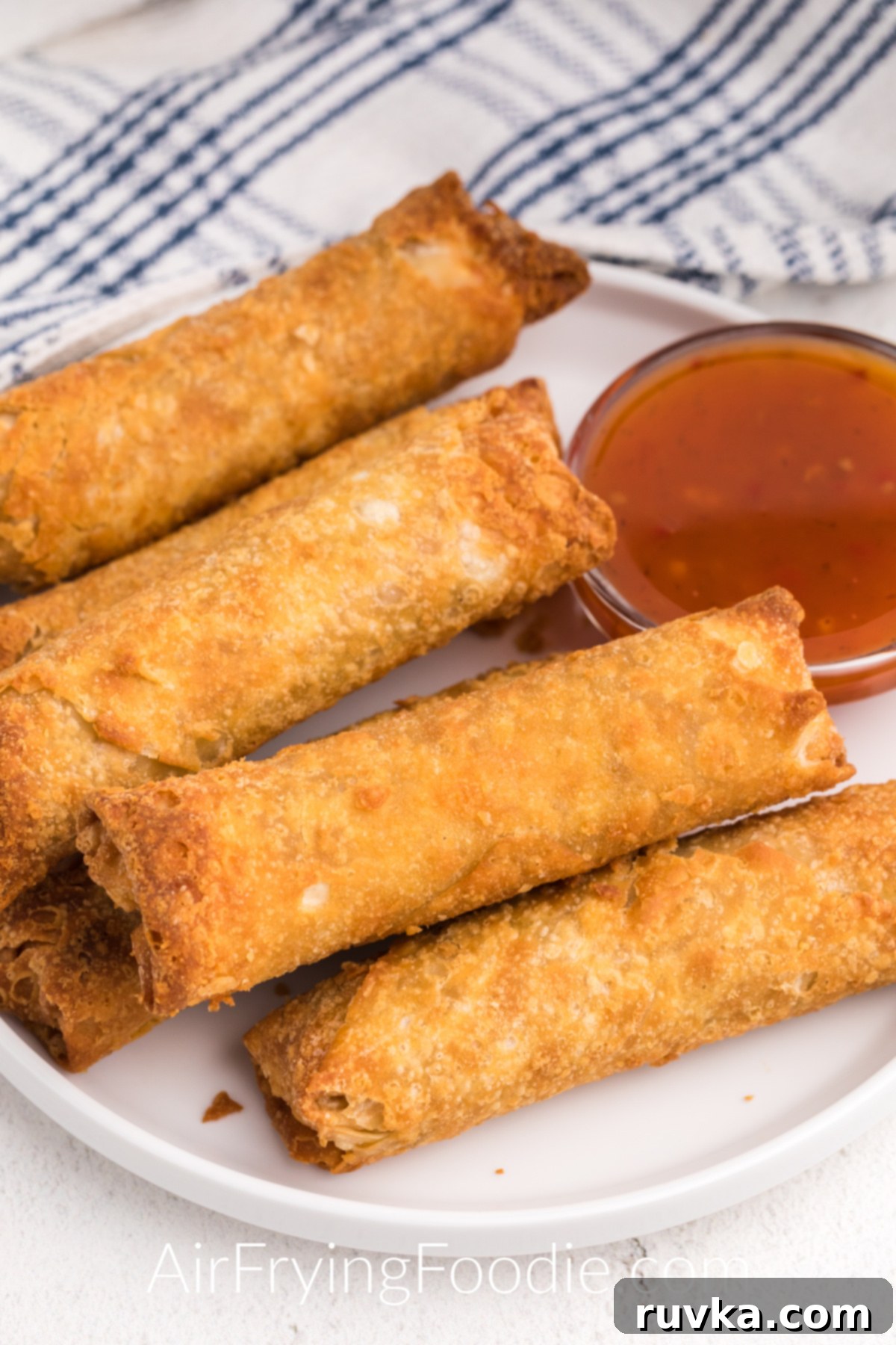 Crispy Frozen Egg Rolls in Air Fryer 6 Crispy cooked golden brown frozen egg rolls made in the air fryer served on a white plate with dipping sauce.