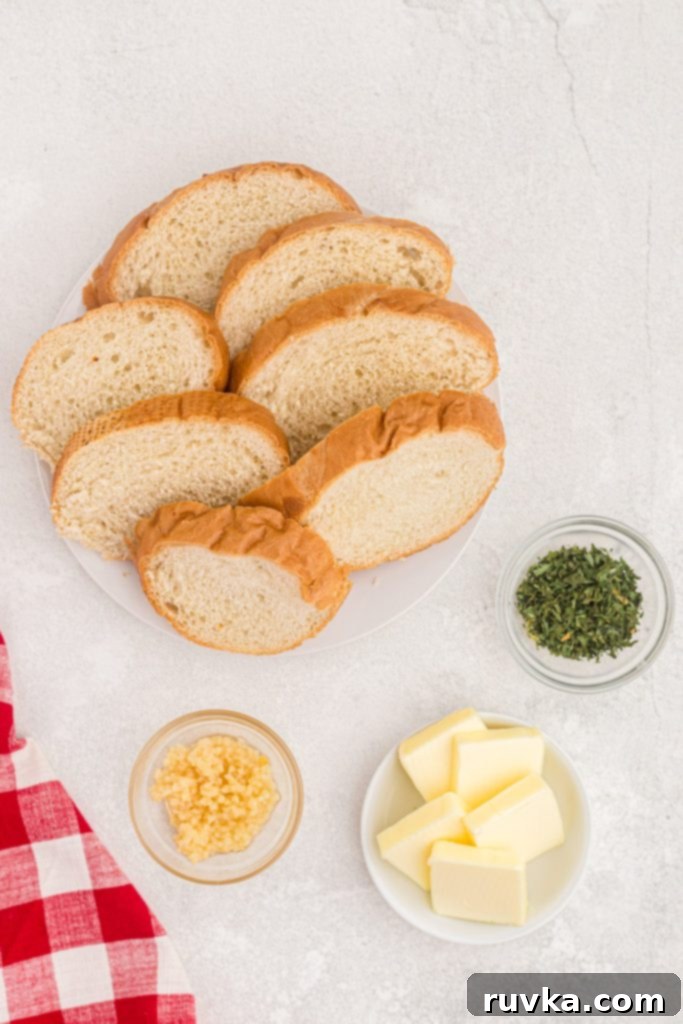 Perfect Air Fryer Garlic Bread 3 Ingredients to make garlic bread, including a loaf of bread, a stick of butter, several cloves of garlic, and a container of parsley flakes, laid out on a kitchen surface.