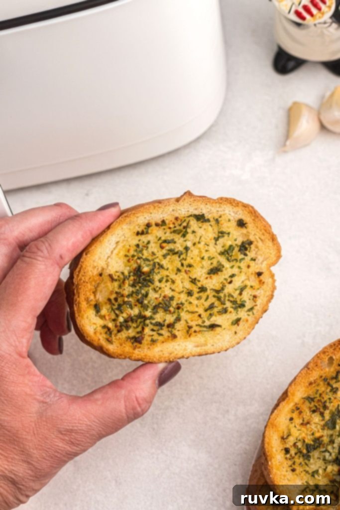 Perfect Air Fryer Garlic Bread 7 A perfectly golden, crispy slice of garlic bread being held in front of a modern air fryer, ready to be enjoyed.