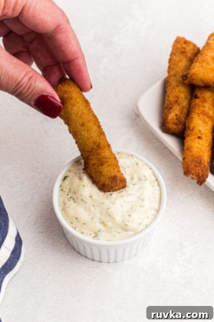 Crispy Air Fryer Fish Sticks 7 Golden breaded crispy fish stick being dipped into tartar sauce dish.