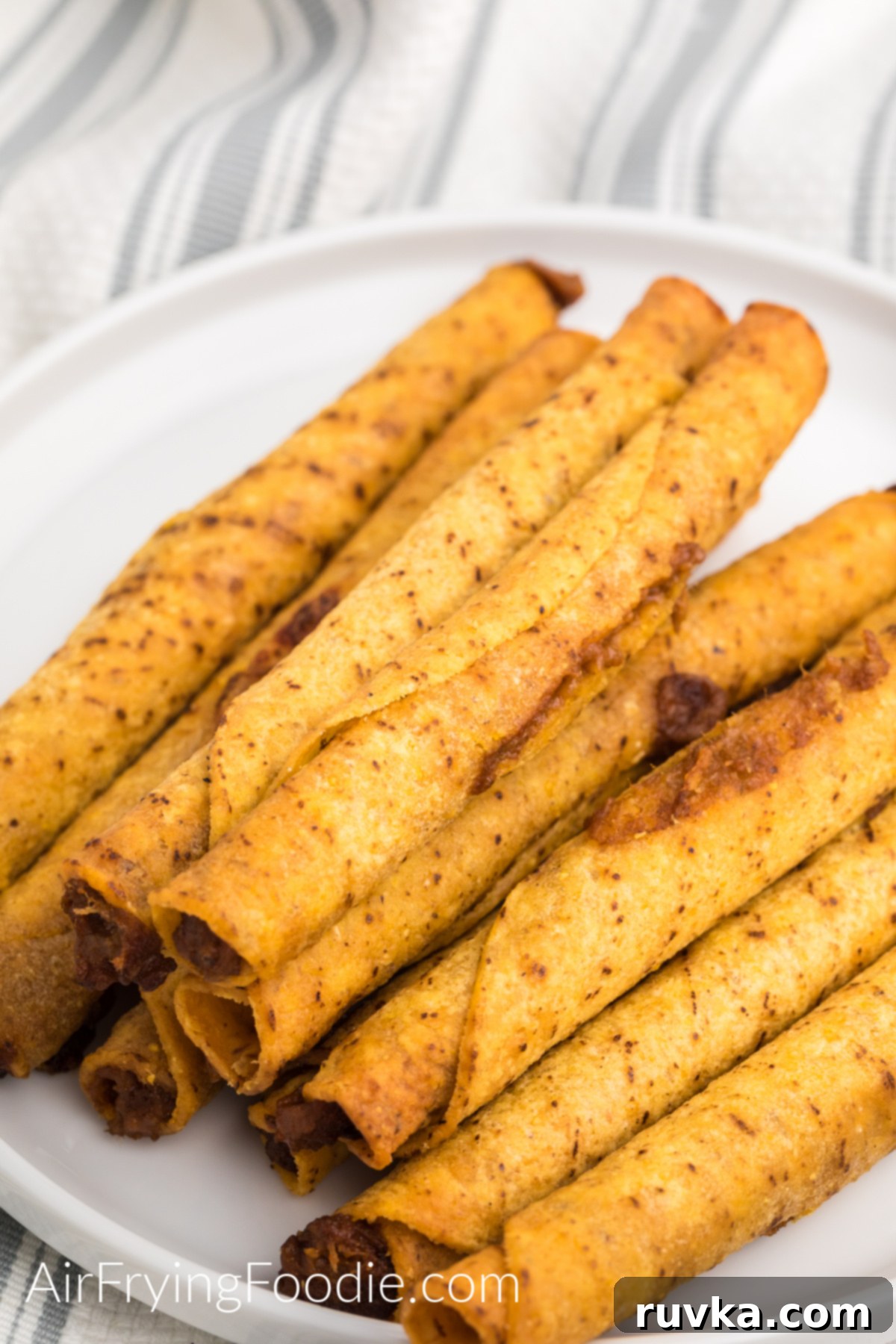 Crispy Air Fryer Frozen Taquitos 2 Taquitos cooked in the air fryer from frozen and served on a white plate.