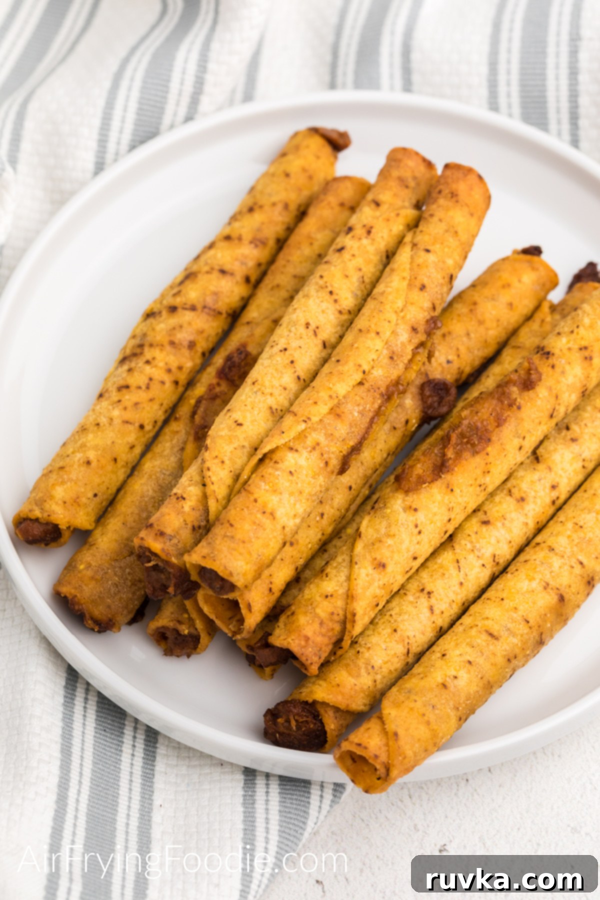 Crispy Air Fryer Frozen Taquitos 6 Cooked taquitos on a white plate and ready to serve.