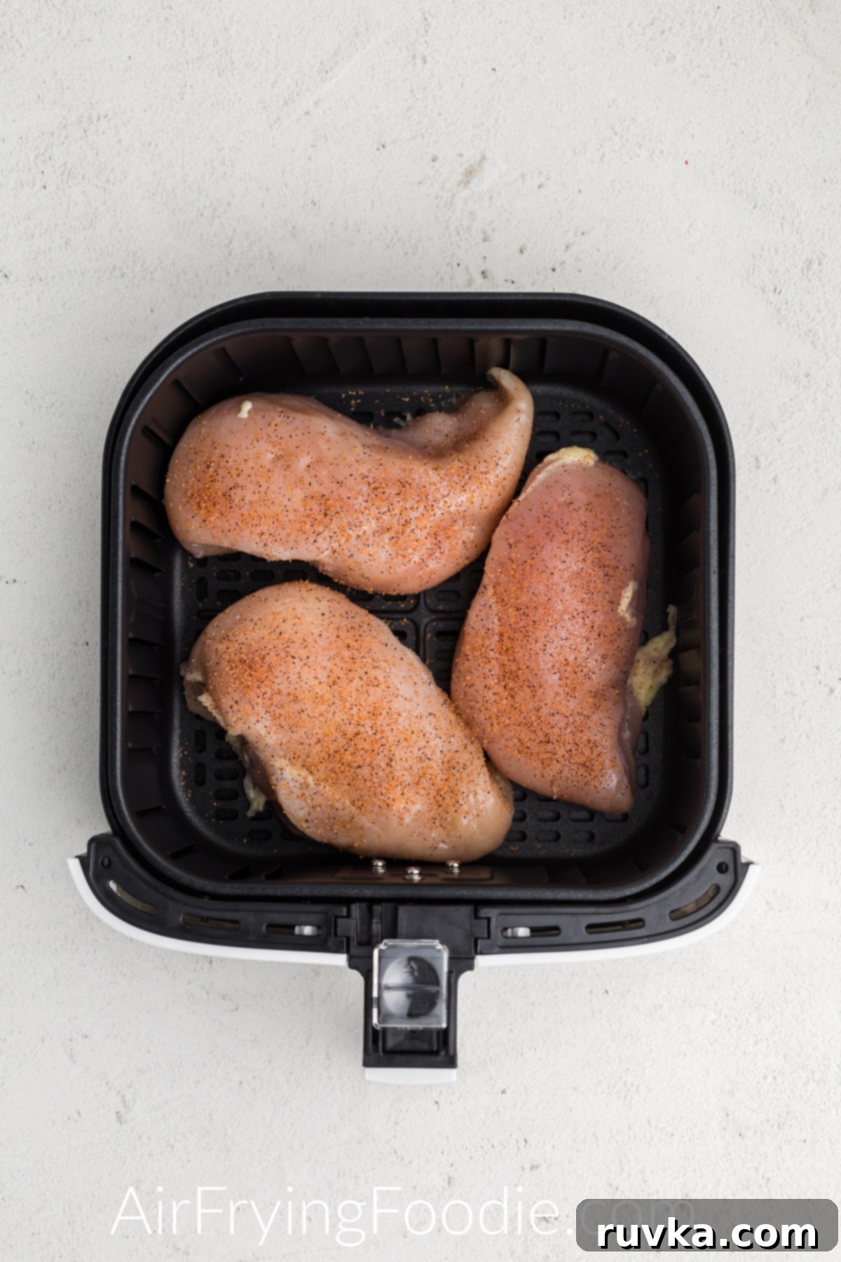 Perfect Air Fryer Frozen Chicken Breast 3 frozen chicken breasts seasoned and placed in a single later in the air fryer basket.