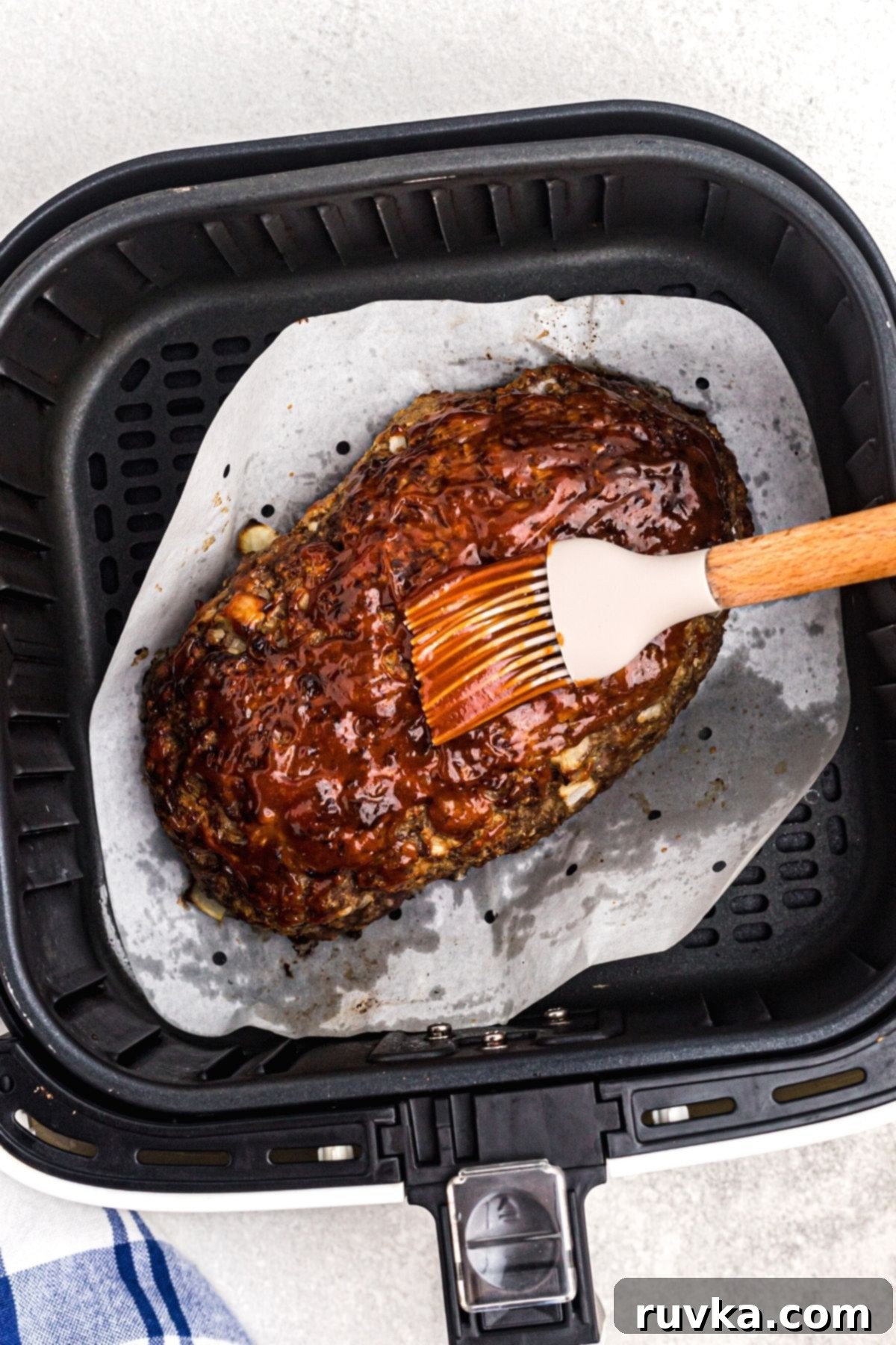 Easy Air Fryer Meatloaf 7 Brushing sauce to top meatloaf in the air fryer basket.