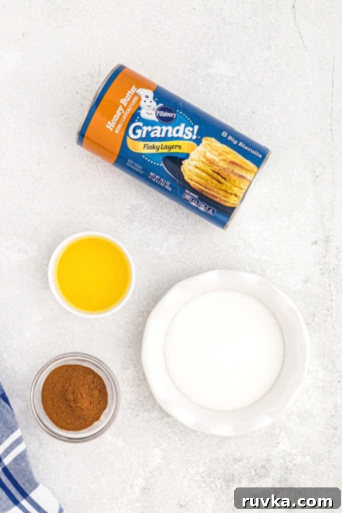Air-Fried Donut Delights 3 All the essential ingredients for making quick air fryer biscuit donuts are neatly arranged in small bowls on a pristine white marble table. The setup includes a can of flaky biscuit dough, a bowl of melted butter, and a blend of granulated sugar and cinnamon, ready for assembly.