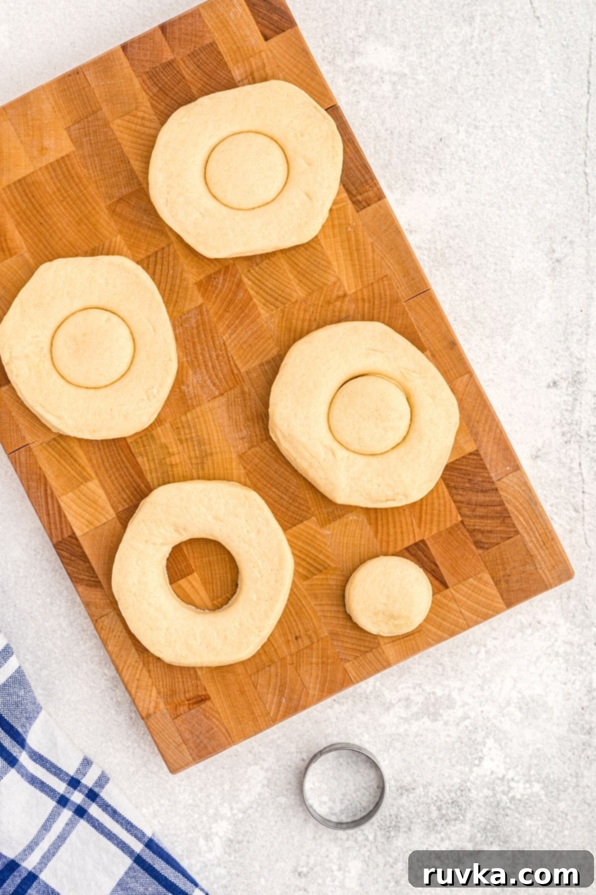 Air-Fried Donut Delights 4 Biscuit dough rounds are shown on a cutting board, with small circular centers being removed using a donut cutter, preparing them for the air fryer. This step ensures classic donut shapes and also yields delicious donut holes.