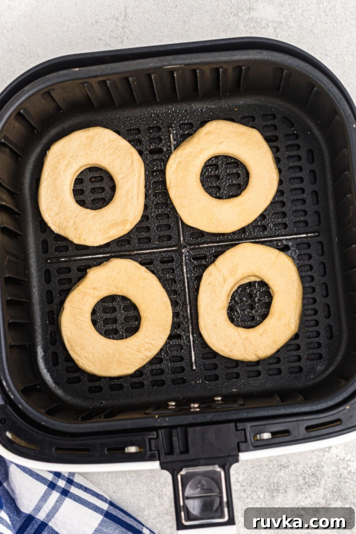 Air-Fried Donut Delights 5 Several uncooked biscuit donuts are carefully placed in the basket of an air fryer, arranged in a single layer to ensure even cooking. The basket is lightly sprayed, indicating preparation for a no-mess air frying experience.