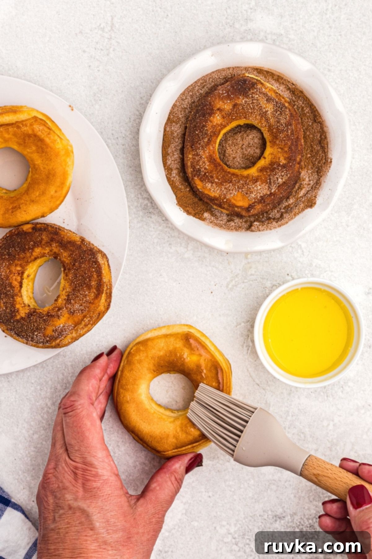 Air-Fried Donut Delights 7 A hand is shown brushing a freshly air-fried donut with melted butter, preparing it for a generous coating of cinnamon and sugar. This step highlights the final touches that make these homemade donuts so irresistible.