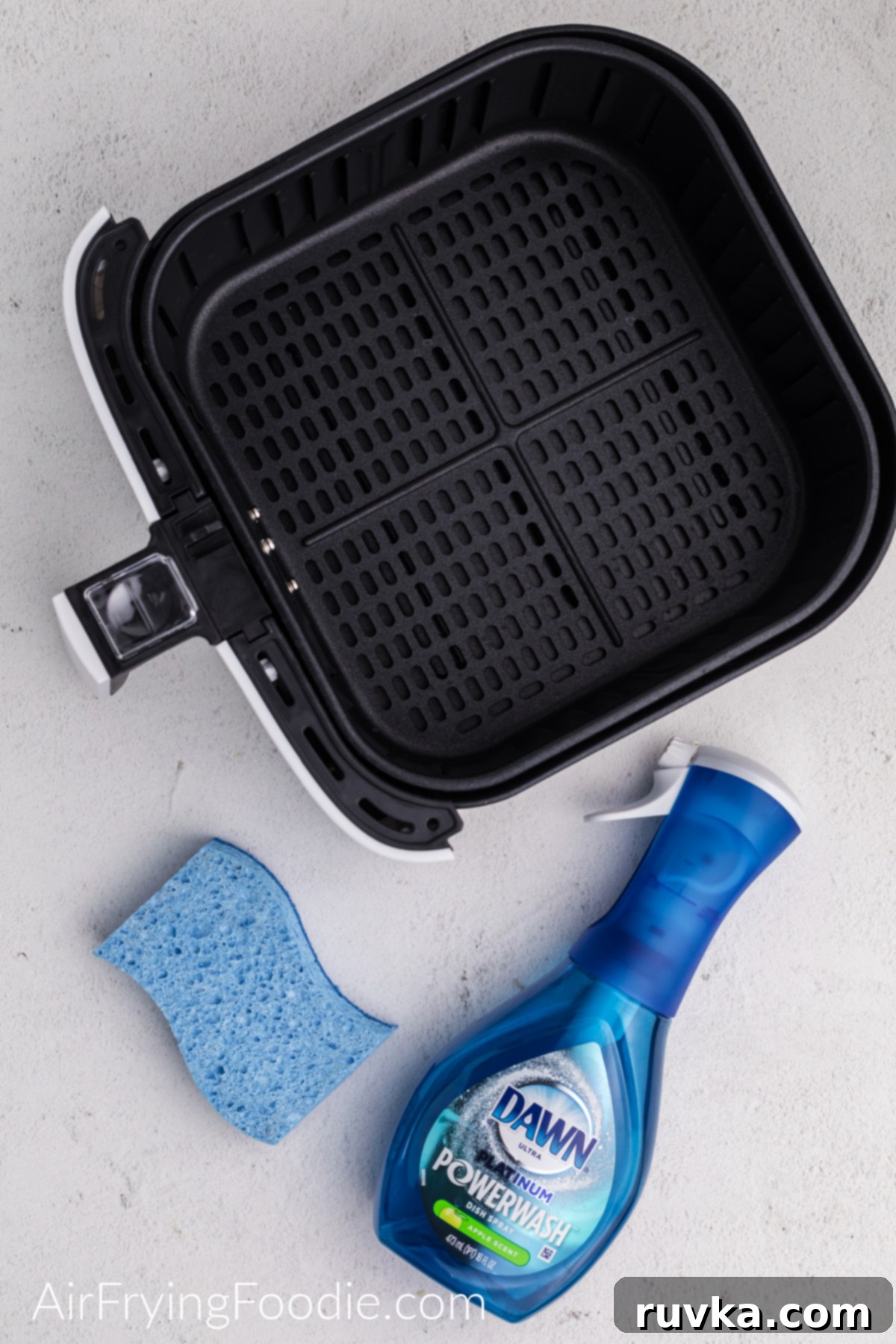 Effortless Air Fryer Cleaning 3 Air fryer basket, sponge, and Dawn powerwash on a white table.