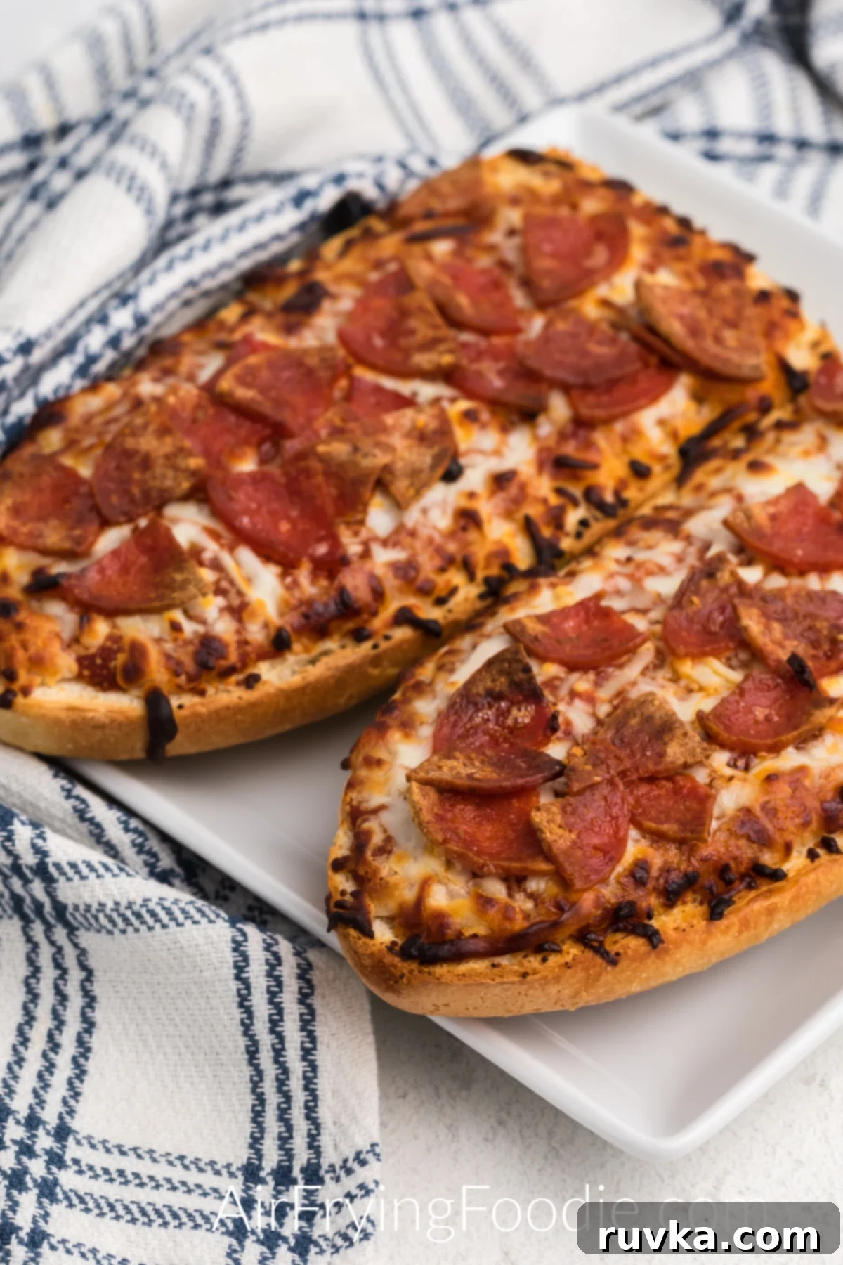 Air Fried French Bread Pizza 2 Fully cooked french bread pizza made in the air fryer on a white plate and ready to eat.