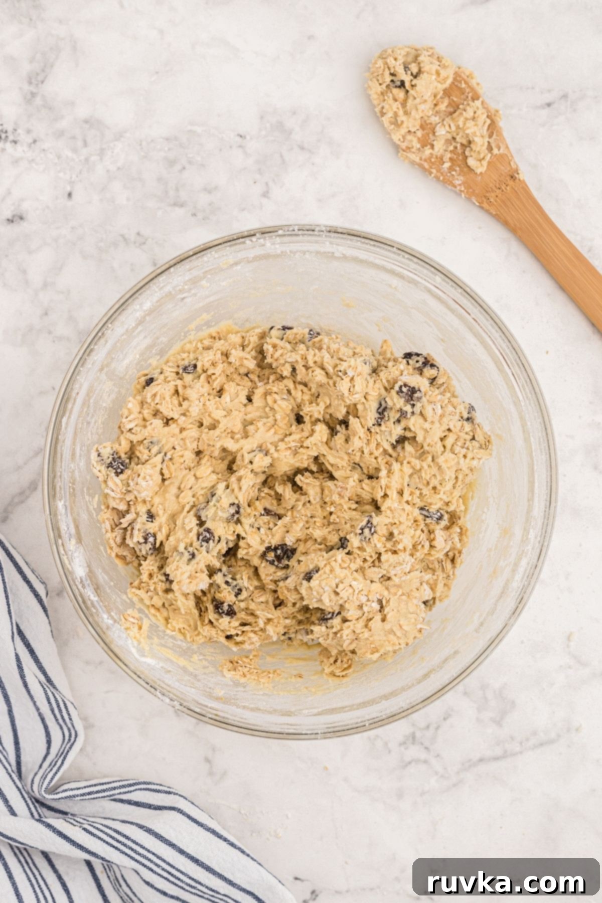 Easy Air Fryer Oatmeal Raisin Cookies 5 Oatmeal raisin cookie dough mixed in a clear glass bowl on a marble table.