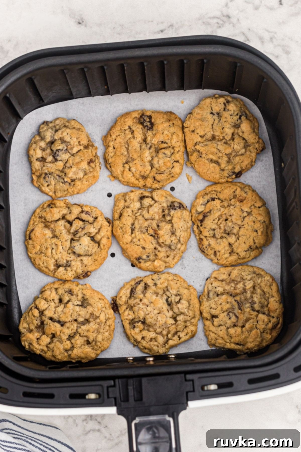 Easy Air Fryer Oatmeal Raisin Cookies 7 Golden brown oatmeal cookies in the air fryer basket after being cooked.