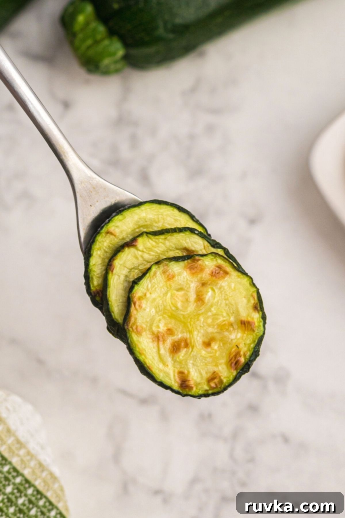 Golden Crispy Air Fryer Zucchini 7 Fork serving cooked zucchini slices from a dish, garnished with fresh lemon.