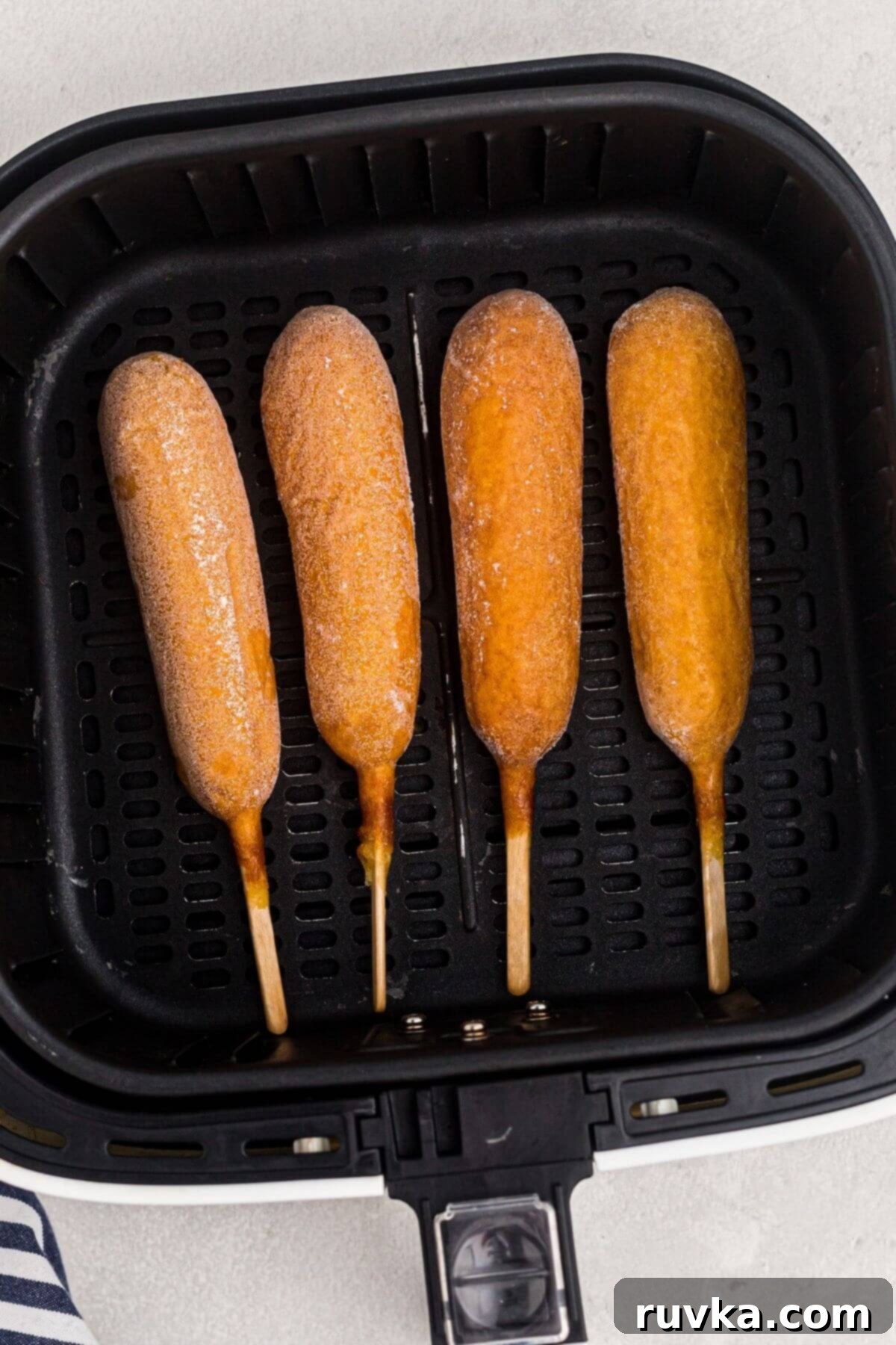 Golden Crispy Air Fryer Corn Dogs 4 Frozen corn dogs side by side in the air fryer basket.
