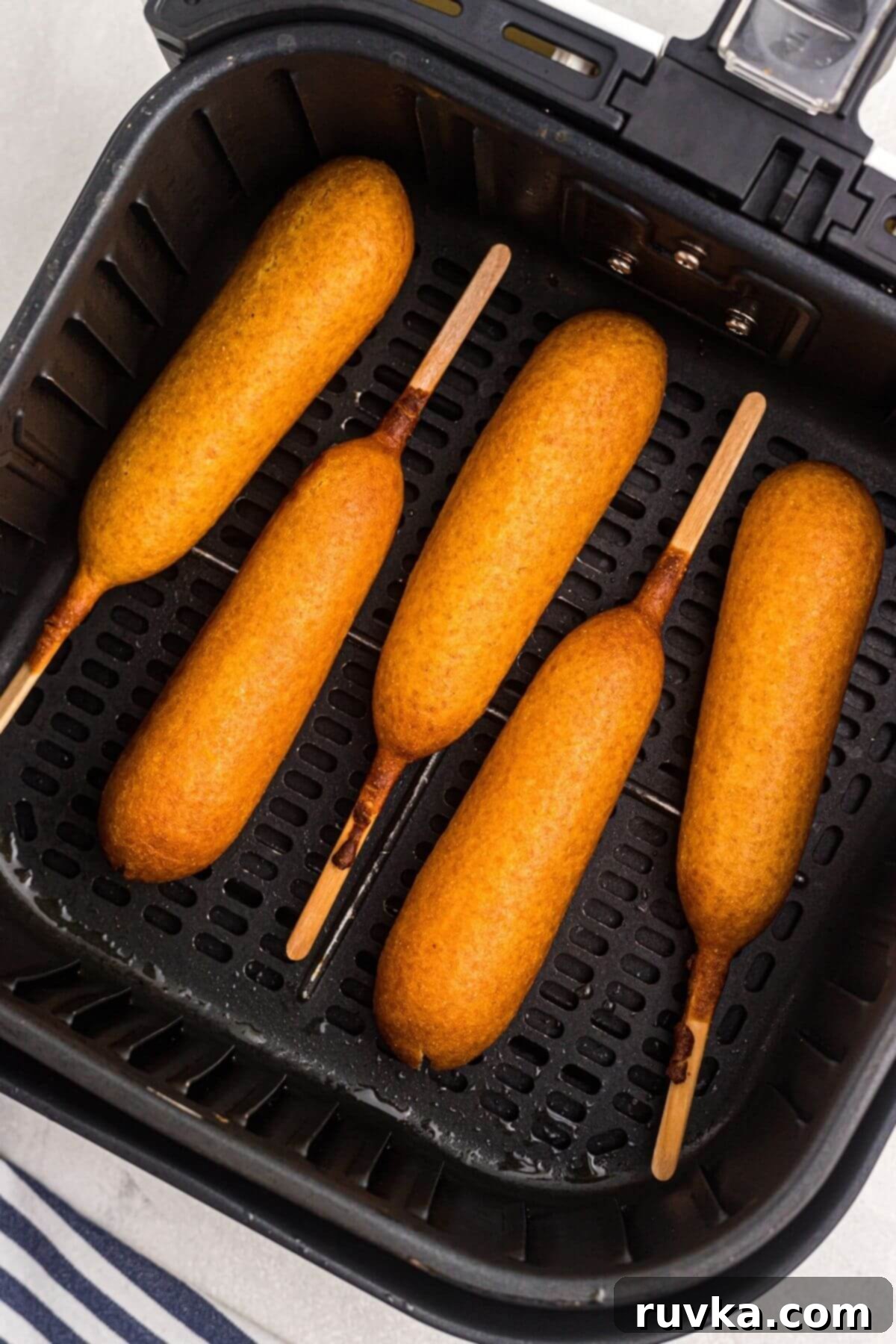 Golden Crispy Air Fryer Corn Dogs 5 Four crispy, golden corn dogs in the basket of the air fryer.