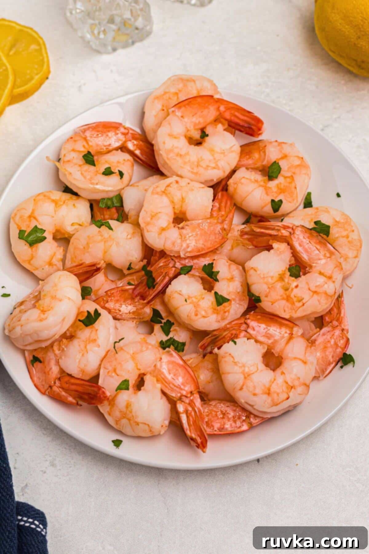 Easy Air Fryer Frozen Shrimp 2 Orange shrimp after being cooked in the air fryer and served on a white plate with lemon wedges and dipping sauce.